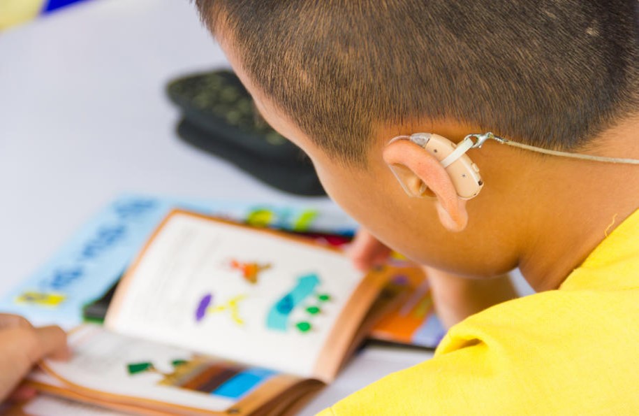 A child wearing a hearing aid device while looking at an instructional book