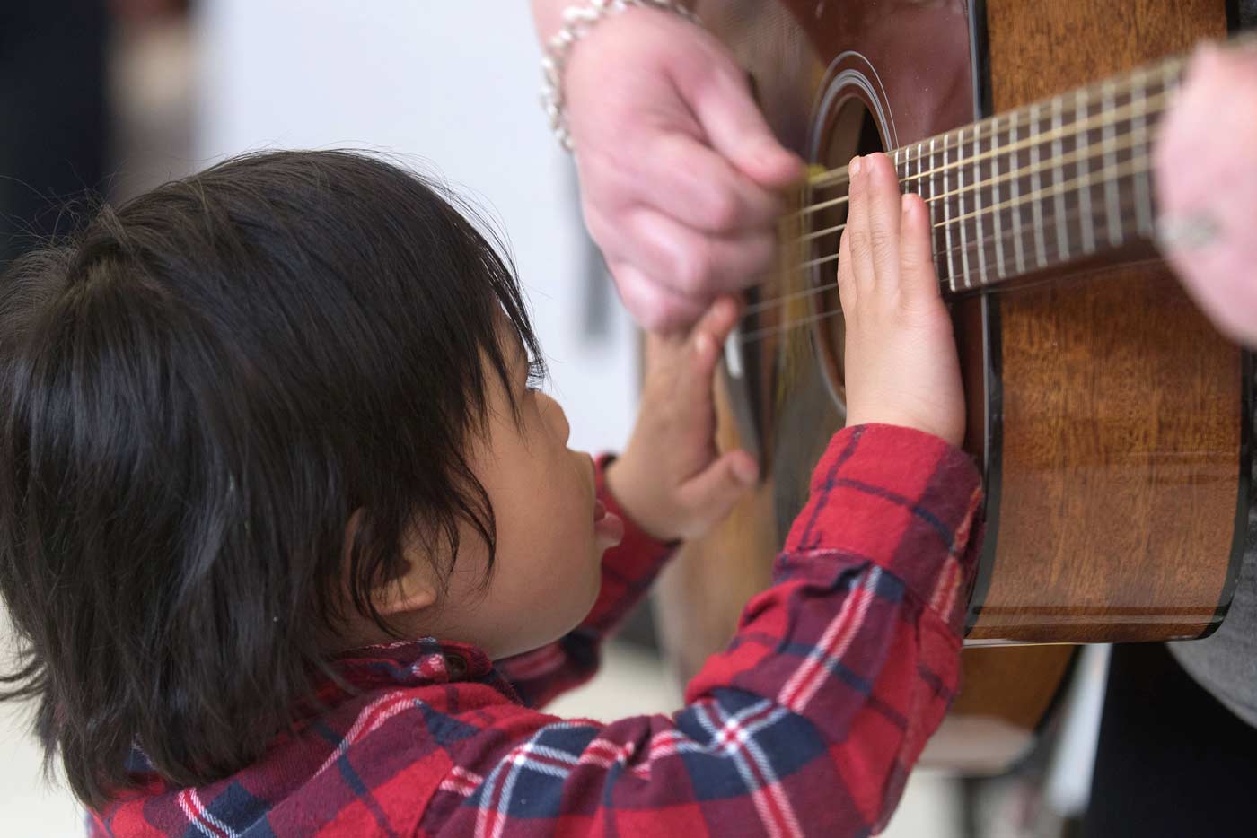 Young student strumming guitar while adult holds it