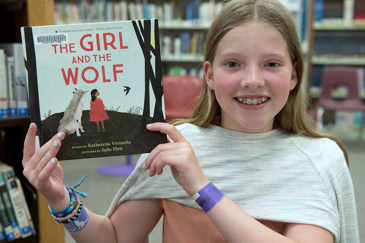 Student smiling and holding up book entitled “The Girl and the Wolf”