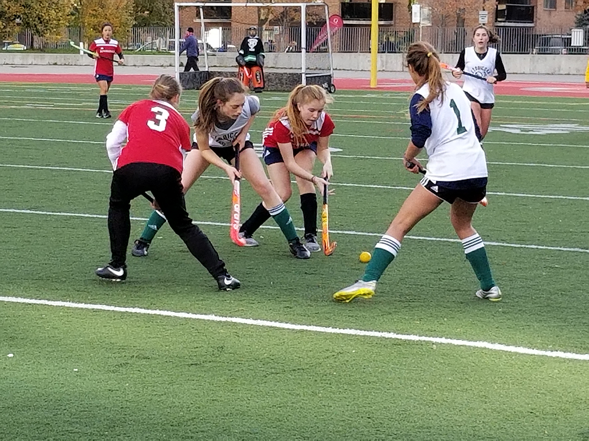 Four female athletes playing field hockey