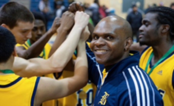 Coach Athony Miller smiles at the camera with his team in a huddle.